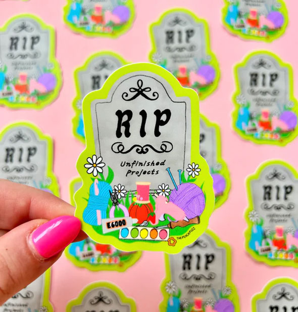 Model's hand holds an RIP Unfinished Projects headstone sticker in front of others like it in the background