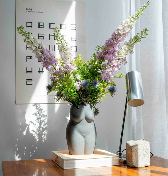 Nude form vase holds a bouquet of fresh florals in a sunny home office setting