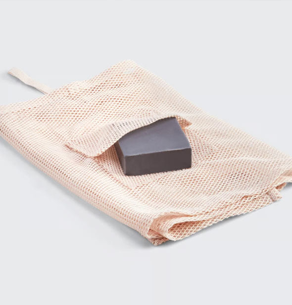 Folded light pink mesh washcloth with charcoal soap bar inserted into built-in pocket