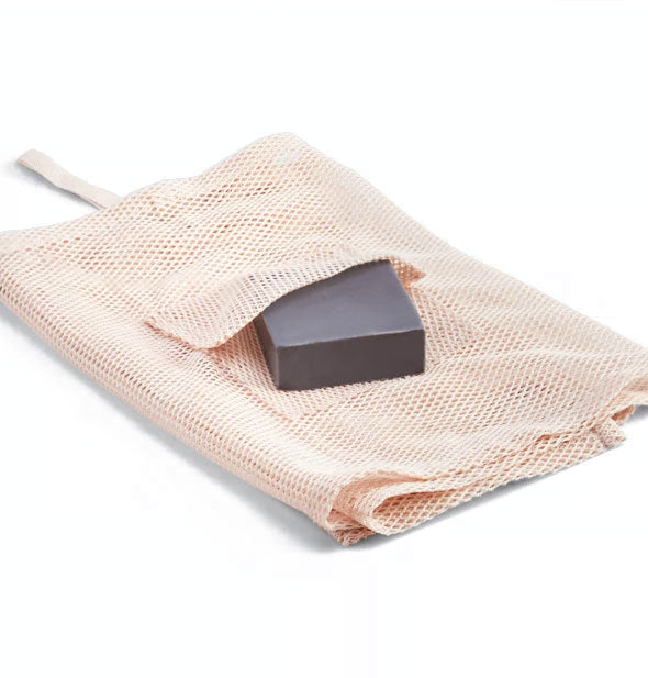 Folded light pink mesh washcloth with charcoal soap bar inserted into built-in pocket