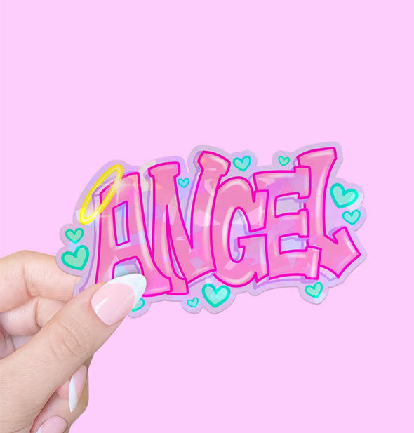 Model's hand holds a sticker that says, "Angel" in pink graffiti-style lettering surrounded by blue hearts with a yellow halo hanging off the "A"