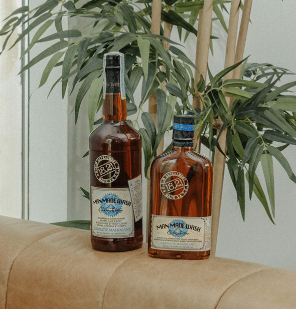 18-ounce and liter-sized bottles of 18.21 Man Made Wash rest on the arm of a couch with exotic plant in the background