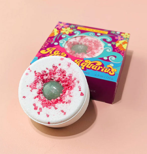 Age of Aquarius bath bomb removed from packaging is a white disc shape with pink crystals and an embedded green aventurine gemstone
