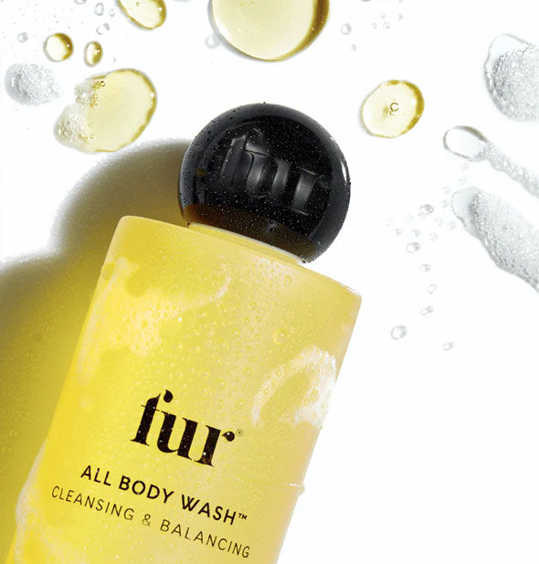 Bottle of Fur All Body Wash on its side is covered in lather and surrounded by golden cleanser droplets