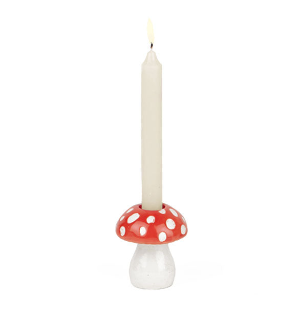 Red and white spotted mushroom candle holder holds a lit white taper candle