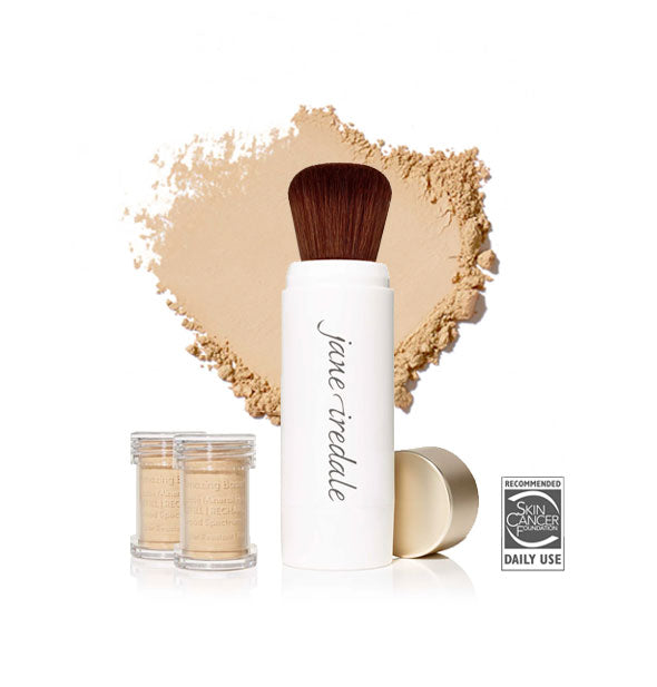 White Jane Iredale powder brush with gold cap removed and set to the side, two refill canisters nearby, and an enlarged product sample in the background in shade Amber