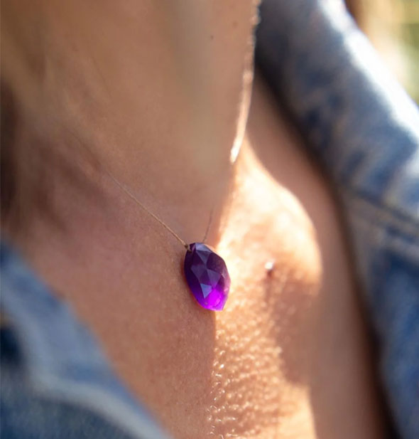 Model wears a faceted purple amethyst stone necklace partially backlit by sunlight