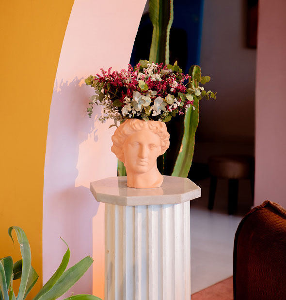Terracotta apollo head vase on a columnar pedestal holds a bouquet of flowers