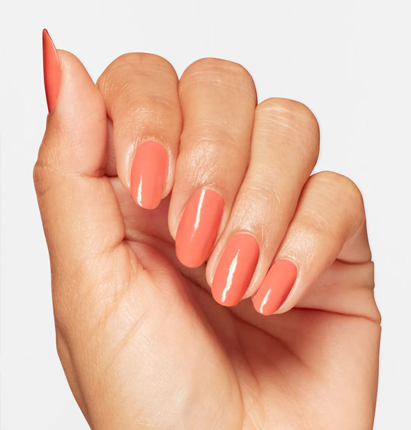 Model's hand wears a pinkish-orange shade of nail polish