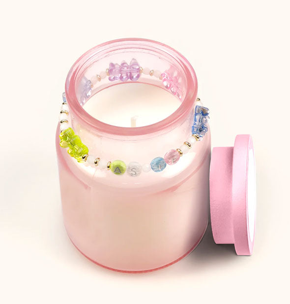 Opened pink glass jar candle with "As If" beaded bracelet around its neck