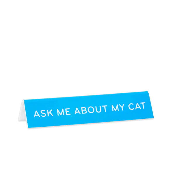 Recangular blue desk sign says, "Ask me about my cat" in white lettering