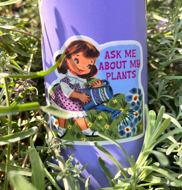 Ask Me About My Plants sticker on a purple water bottle resting in a bed of greens