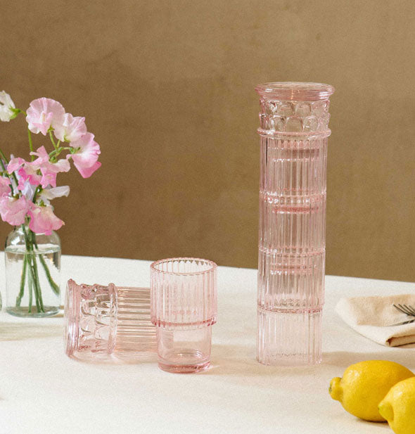 Stackable pink column glasses on a tabletop with lemons, flowers, and utensils