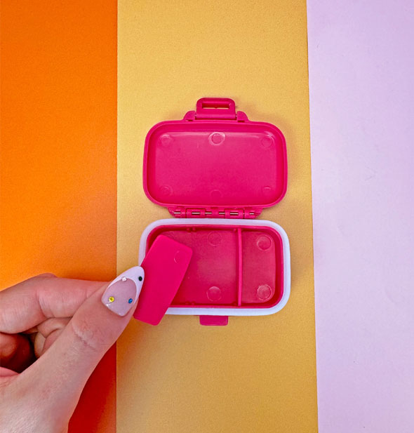 Model removes a divider from the inside of a pink pill case