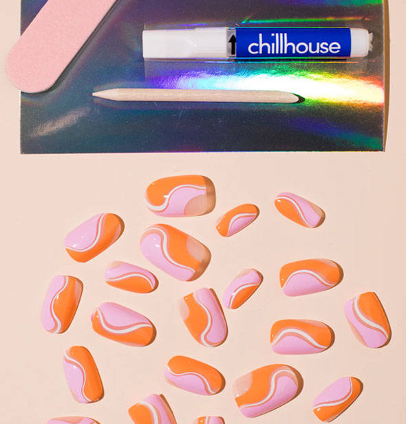 Contents of the Chillhouse Babs on the Beach manicure set: Pink file, glue tube, wooden cuticle pusher, and scattered nails in varying sizes featuring a wavy orange, pink, and white design