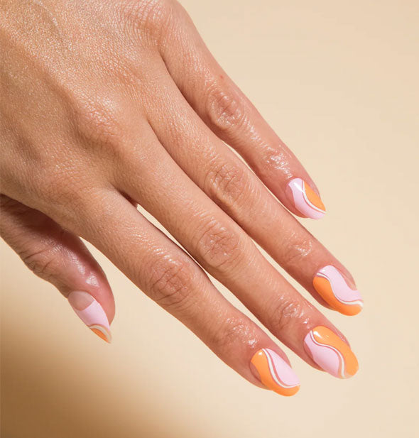 Model's hand wears a wavy pink, white, and orange press-on nail manicure design