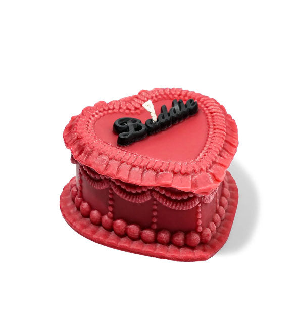 Red heart-shaped cake candle designed to resemble a cake with ornate frosting and the word, "Baddie" on top in black script lettering