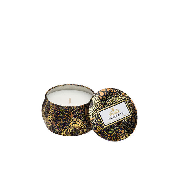 A small unlit candle inside a rounded tin with metallic floral design and matching lid set to the side