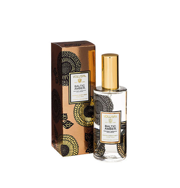 Floral-patterned clear glass bottle of Voluspa Baltic Amber Room & Body Mist next to bronze gift box with black and gold floral pattern