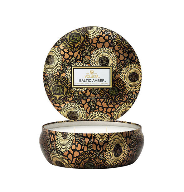 Round gold, amber, and black floral patterned Voluspa Baltic Amber candle tin with lid removed and positioned upright behind the tin