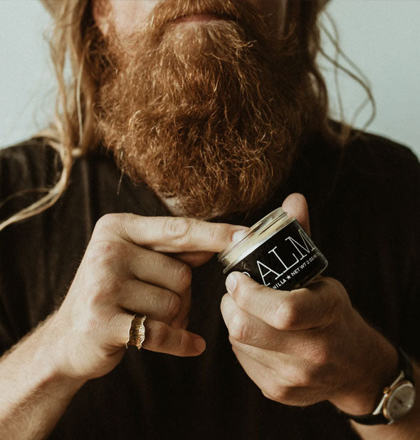 Model dips a finger into an opened jar of Balm for beards