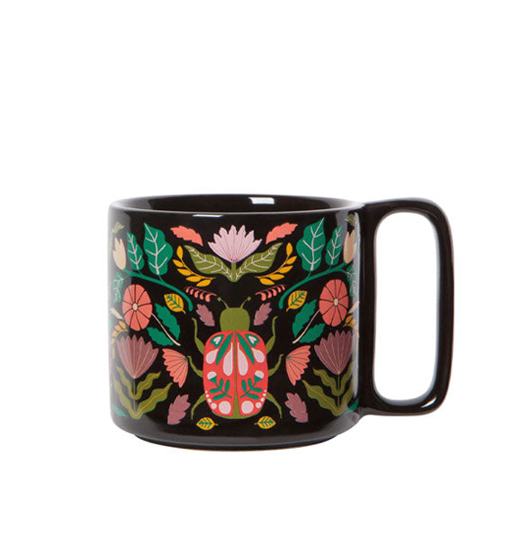 Somewhat stout black coffee mug with rectangular handle features colorful, intricate designs of flowers, leaves, and vines around a central scarab beetle