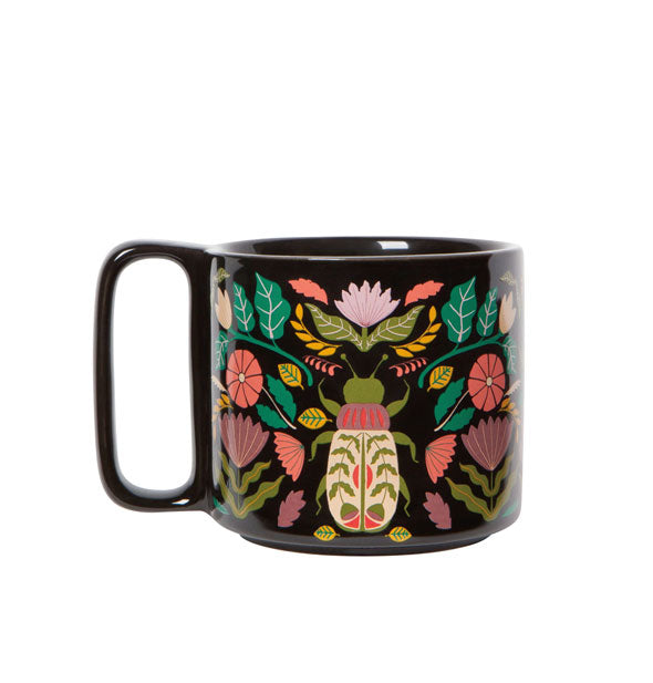 Somewhat stout black coffee mug with rectangular handle features colorful, intricate designs of flowers, leaves, and vines around a central scarab beetle