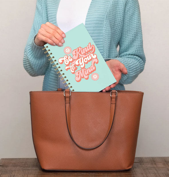 Model takes a Be Kind to Your Mind notebook out of a brown handbag
