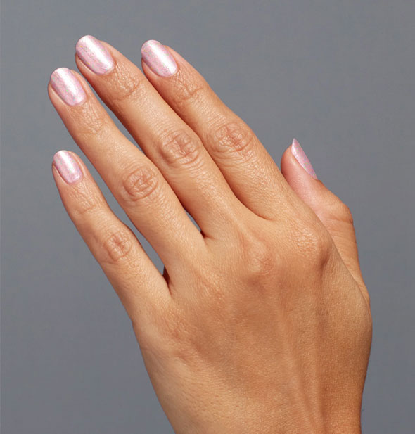 Model's hand wears a light shimmery shade of pink nail polish