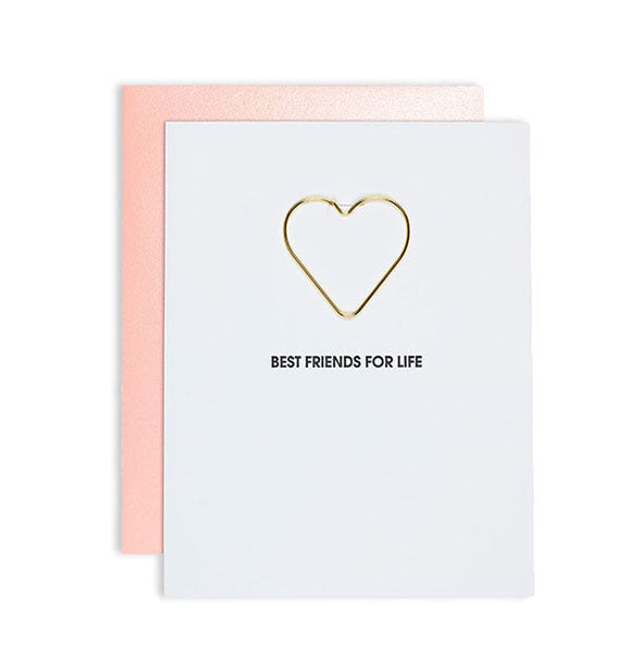 White greeting card imprinted “Best Friends for Life“ with gold heart-shaped paper clip attached and light coral envelope behind.