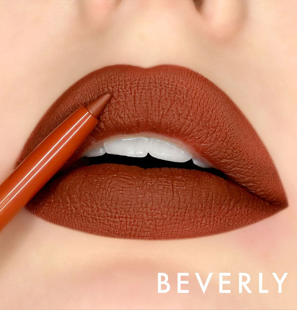 Model's lips wear shade Beverly of Kara Beauty Line Up Lip Liner; pencil tip is held up to upper lip
