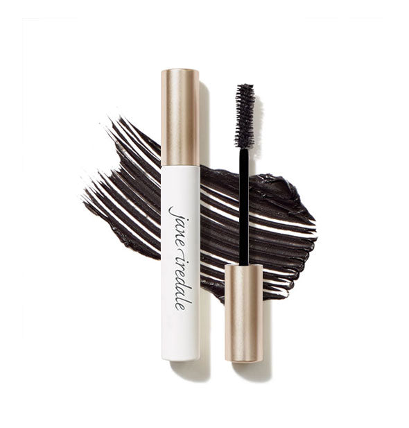 White and gold tube of Jane Iredale mascara with separate spoolie brush applicator cap both rest atop a sample streaked product application in shade Black Ink