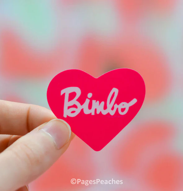Model's hand holds a pink heart-shaped sticker that says, "Bimbo" in white script lettering