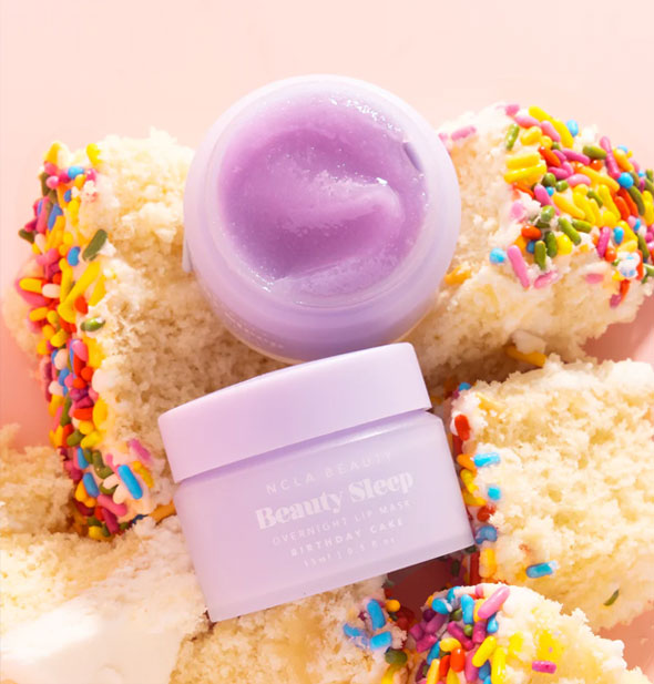 One closed and one opened pot of Birthday Cake NCLA Beauty brand Beauty Sleep Overnight Lip Mask staged with pieces of white cake with rainbow sprinkles
