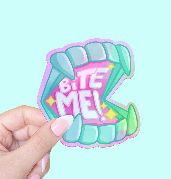 Model's hand holds a sticker designed as a set of blue teeth with vampire fangs inside of which the words, "Bite me!" in white lettering on a pink background are accented by yellow stars