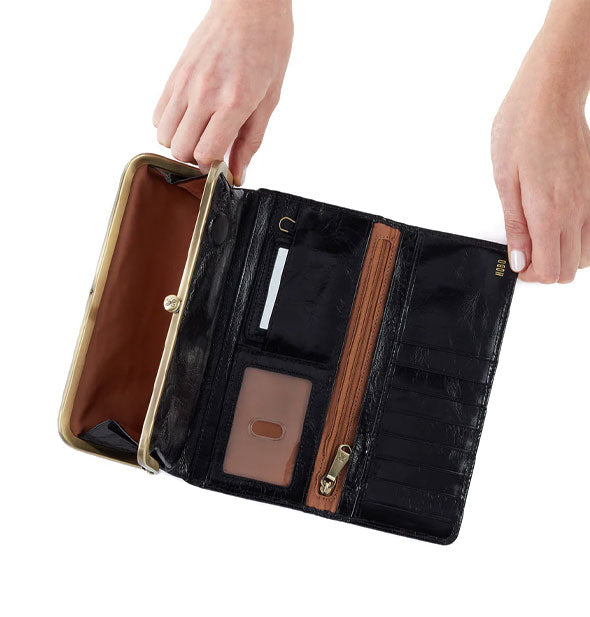 Model's hands hold open a black leather wallet to show storage compartments and brown lining inside