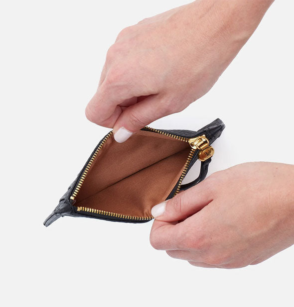 Model's hands hold open a black leather card case wallet with brown interior and gold zipper hardware