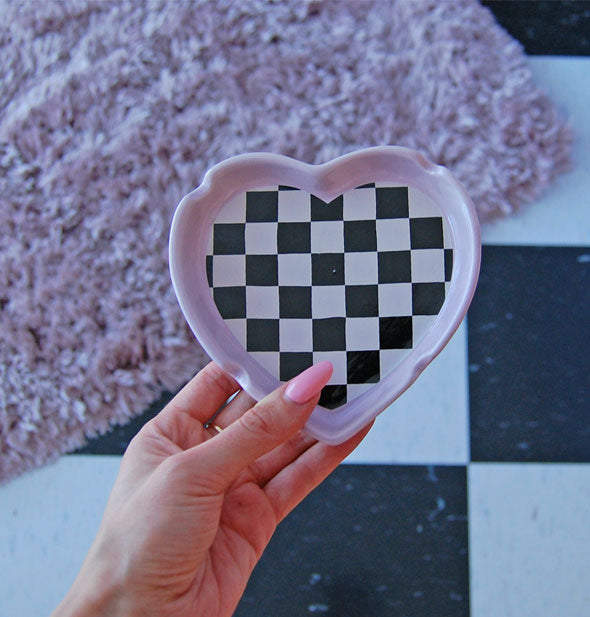 Model's hand holds a heart-shaped checker print ashtray above a matching floor with pink shag rug