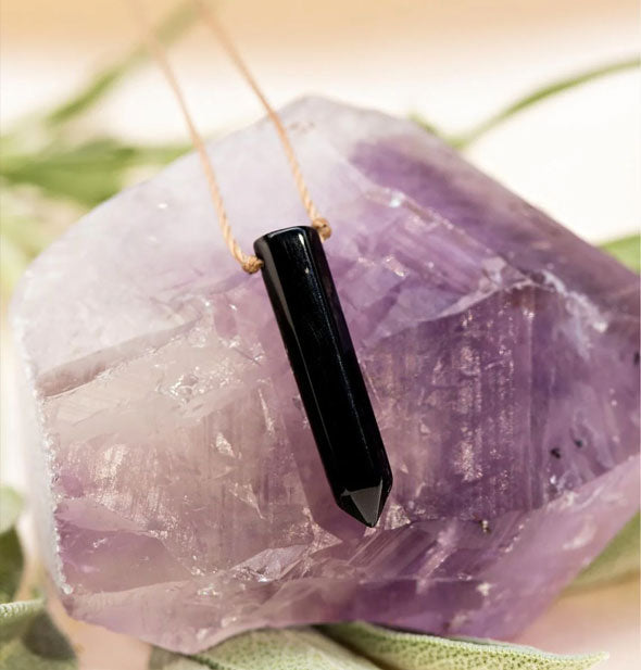 Black onyx point necklace on gold strand rests on a piece of purple amethyst