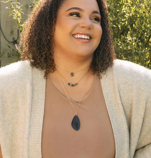 Smiling model wears a black onyx stone necklace at a longer length with other necklaces