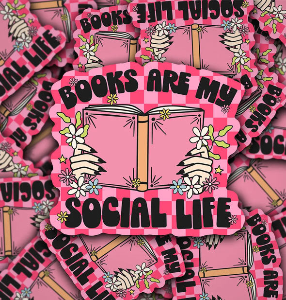 Pile of stickers feature illustration of hands with long nails holding a pink book flanked by flowers on a pink checkered background and the words, "Books are my social life" in black lettering