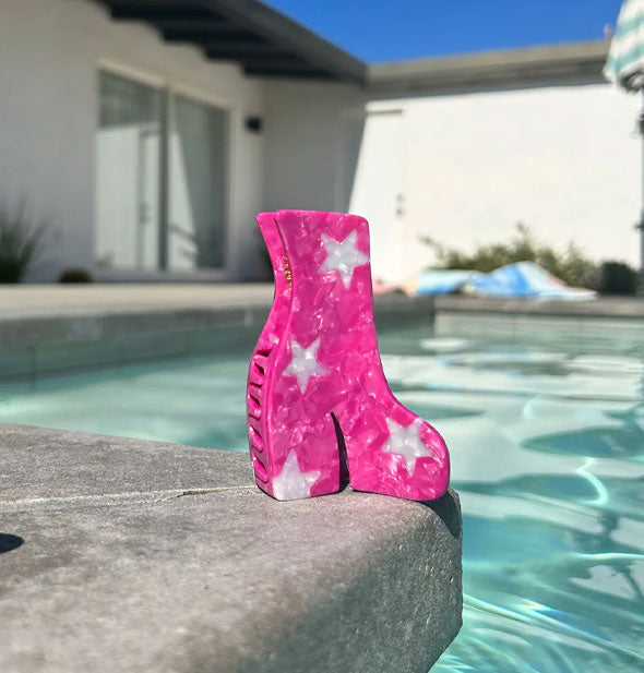 Pink and white star print hair clip rests on the concrete edge of an in-ground pool