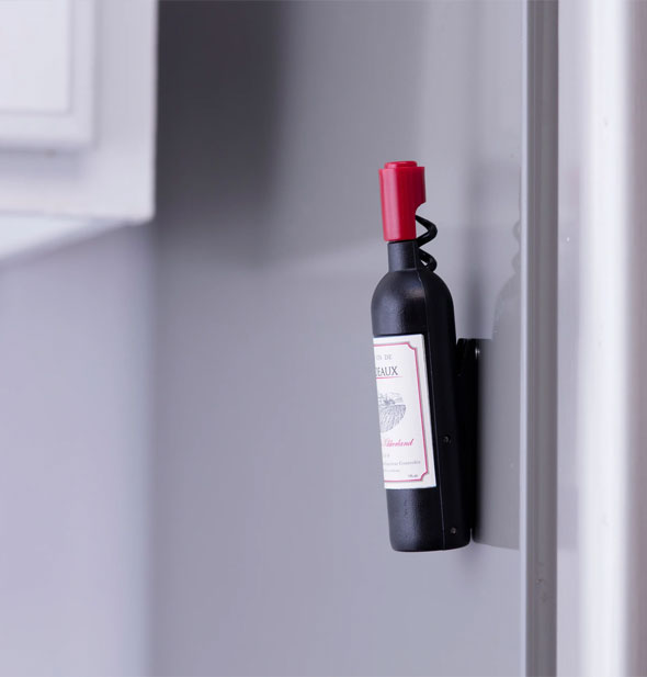 Mini magnetic wine bottle corkscrew is attached to a vertical stainless steel surface