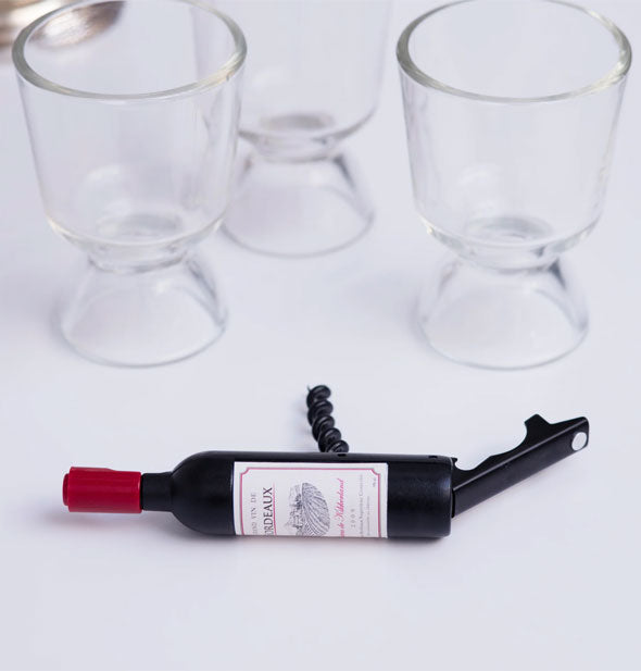Mini wine bottle corkscrew rests on a tabletop with glassware