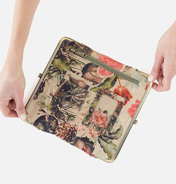 Model's hands hold open a floral wallet to show interior pockets and slots
