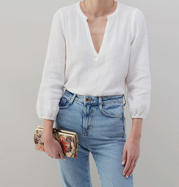 Model wearing jeans and a white shirt holds a floral wallet with gold hardware for size reference