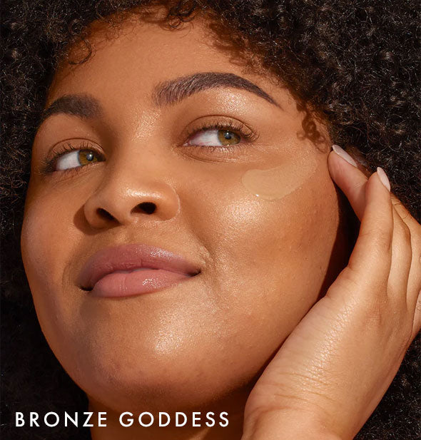 Model applies Coola Rosilliance Tinted Moisturizer Sunscreen in shade Bronze Goddess to cheek