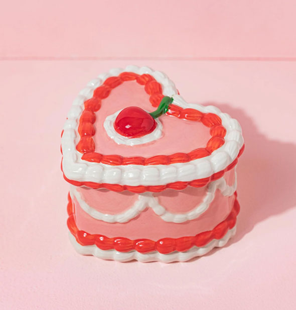 Red, white, and pink heart-shaped ceramic  box designed to resemble a heavily decorated cake with a cherry on top