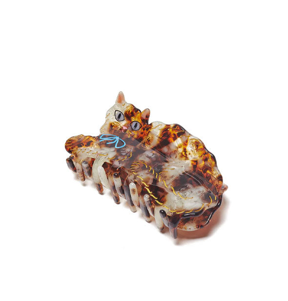 Brown and beige tortoise claw clip resembles a calico cat with blue bow, gold detail accents, and intense-looking eyes