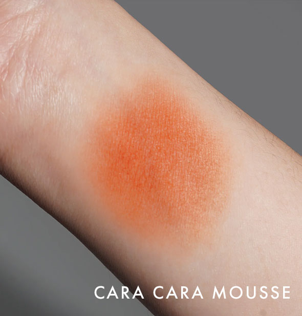 Kara Beauty Soft Serve Lip & Cheek Whip shade Cara Cara Mousse is applied to the inside of a model's wrist